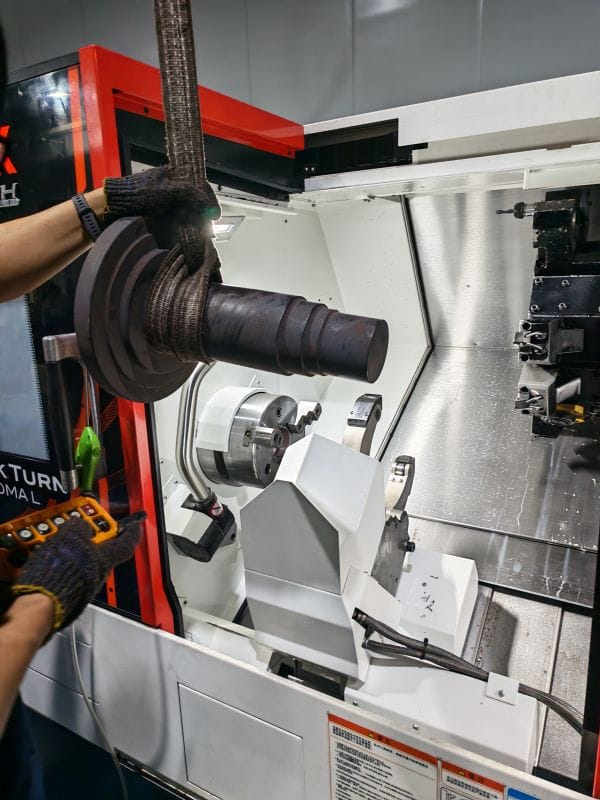 Large forged gear shaft being loaded into a CNC lathe for semi-finish turning