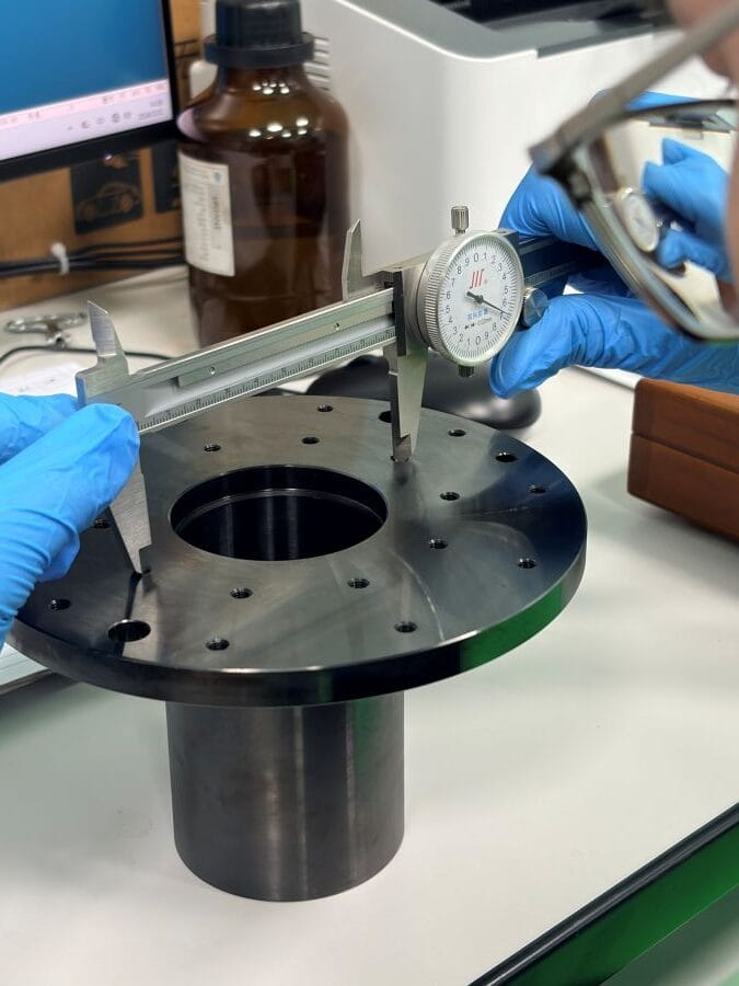 Inspector measuring a machined robotic component with a dial caliper at Weforging